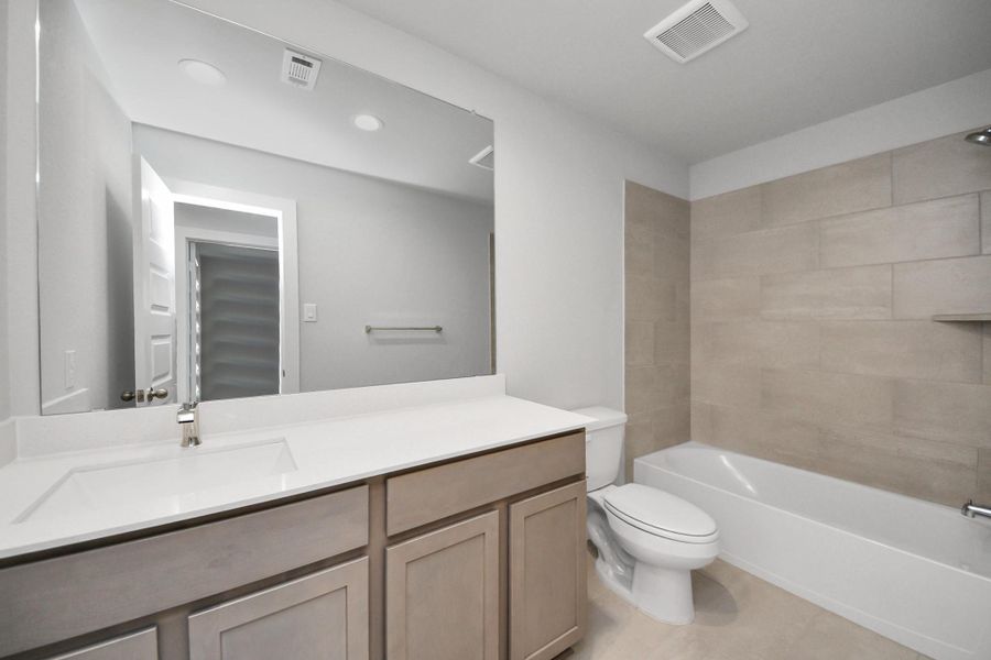 Secondary bath features tile flooring, bath/shower combo with tile surround, light stained wood cabinets, beautiful light countertop. Sample photo of completed home with similar floor plan. Actual colors and selections may vary.