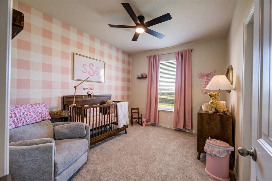 Bedroom featuring wallpapered walls, a crib, carpet flooring, and a ceiling fan