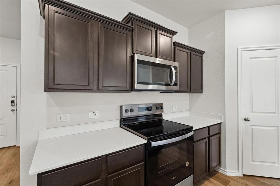 Kitchen featuring dark wood cabinetry, light countertops, a stainless steel over-the-range microwave, and a stainless steel electric range