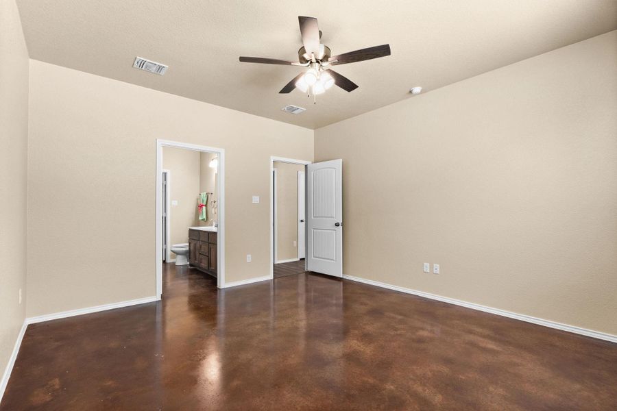 Unfurnished bedroom featuring concrete floors, a ceiling fan, and ensuite bath