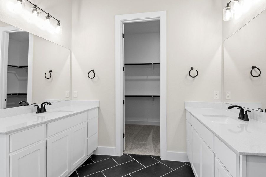 Full bath featuring a spacious closet, two vanities, and dark tile patterned flooring