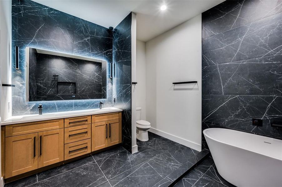 Bathroom with vanity, toilet, a tub to relax in, and tile walls