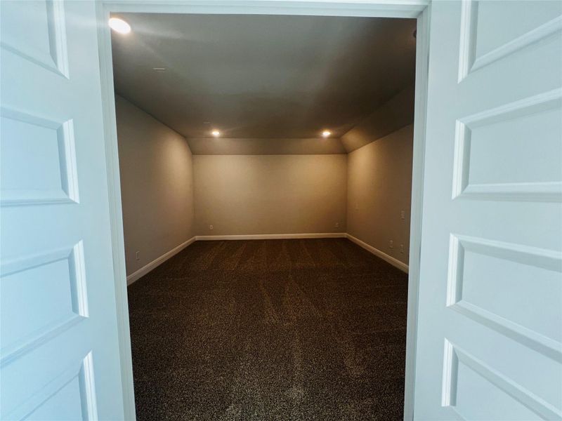 Spare room featuring dark colored carpet, built in shelves, recessed lighting, and vaulted ceiling