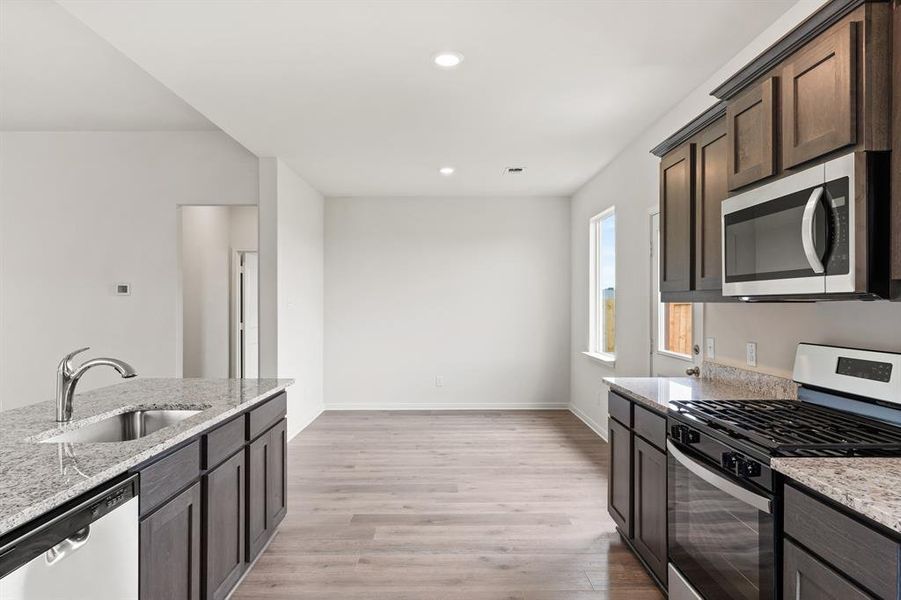 Kitchen featuring stainless steel appliances, light stone counters, dark brown cabinetry, light wood-style floors, and recessed lighting Kitchen featuring stainless steel appliances, light stone counters, dark brown cabinetry, light wood-style floors, and recessed lighting