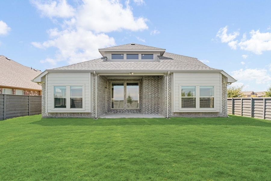 Rear exterior of single-story home with brick and siding, covered patio, large windows, and fenced backyard with green lawn. Rear exterior of single-story home with brick and siding, covered patio, large windows, and fenced backyard with green lawn.