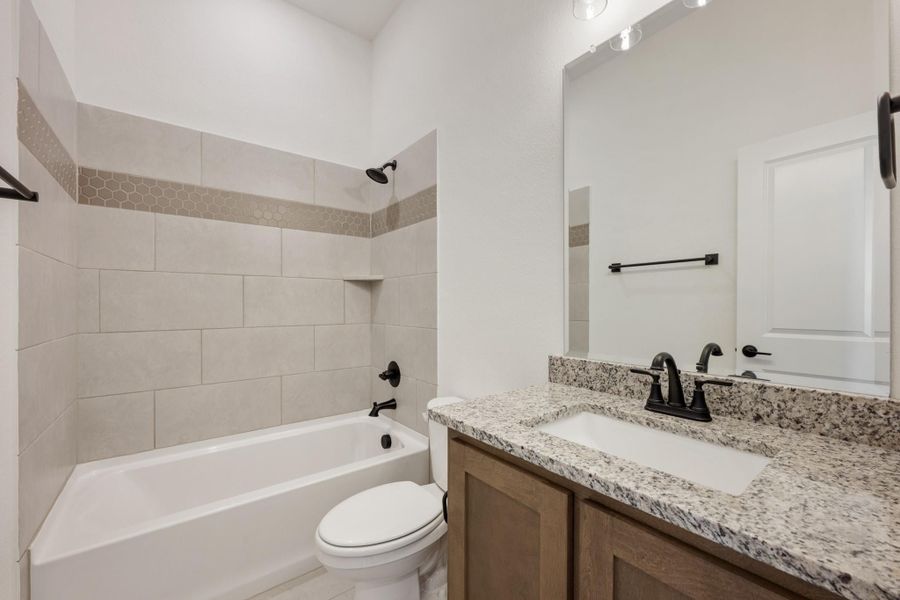 Bathroom with granite vanity, wood cabinets, tiled tub-shower combo, and black fixtures Bathroom with granite vanity, wood cabinets, tiled tub-shower combo, and black fixtures