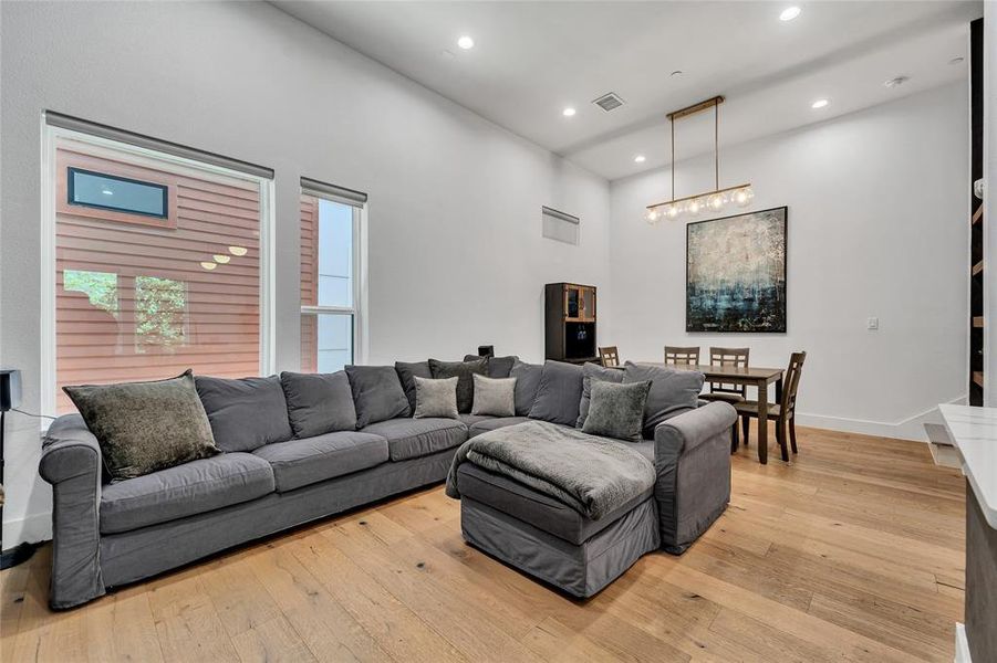 Living room with light wood-style floors, recessed lighting, and a towering ceiling Living room with light wood-style floors, recessed lighting, and a towering ceiling