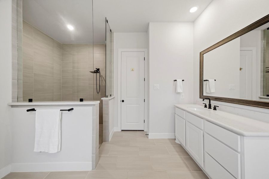 Extended counter space allows for plenty of room to navigate your morning routines. The nearby shower is finished with tile to the ceiling and features a rain shower head paired with a separate spray wand, delivering a luxurious, customizable shower experience. A linen closet sits straight ahead.