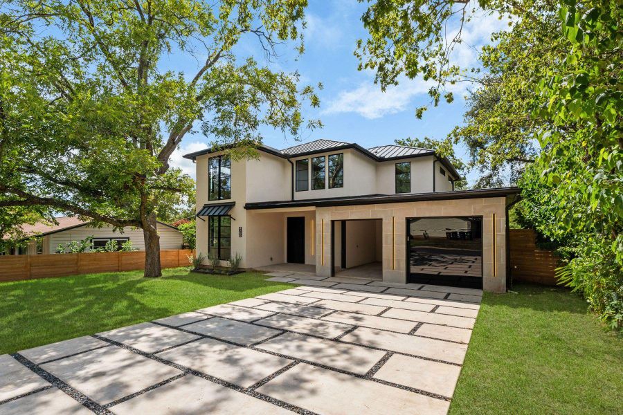 Geometric paver driveway leads to a contemporary two-story residence framed by mature shade trees.