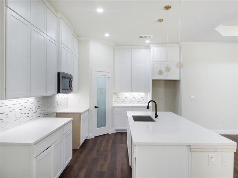 Kitchen with decorative backsplash, white cabinets, pendant lighting, dark wood finished floors, and crown molding Kitchen with decorative backsplash, white cabinets, pendant lighting, dark wood finished floors, and crown molding