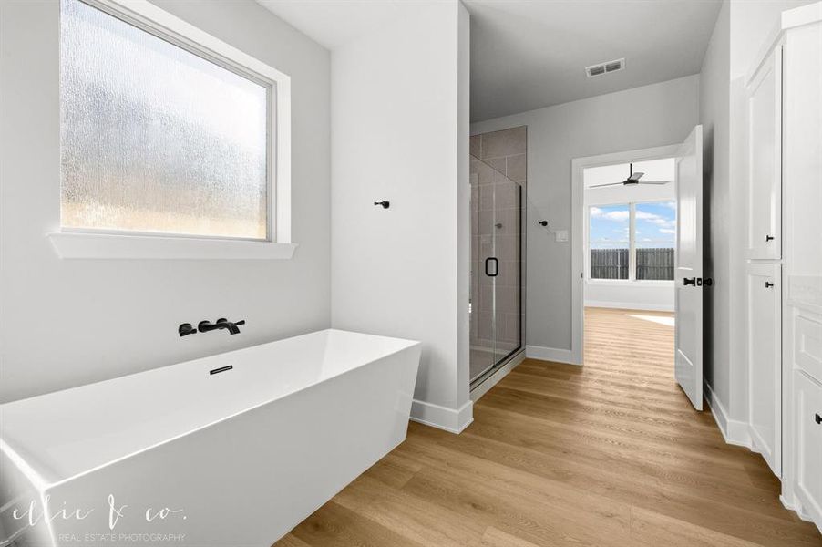 Full bathroom featuring a freestanding tub, a shower stall, light wood-type flooring, and a ceiling fan