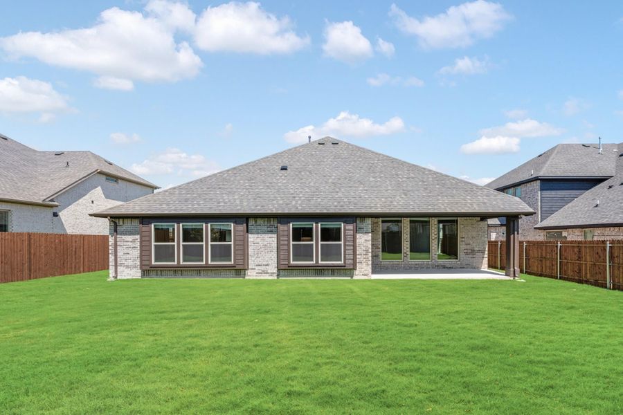 Rear view of single-story brick home with covered patio, large fenced backyard, and green lawn