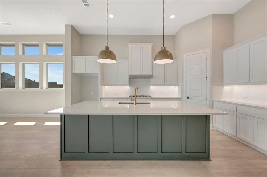 Spacious kitchen featuring a large island with a green paneled base, white countertops, and a gold-finish faucet
