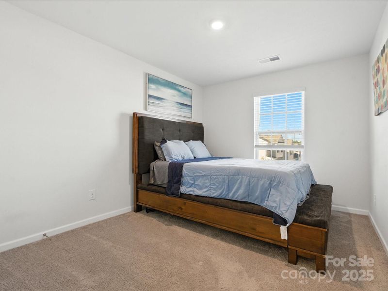 Comfortable secondary bedroom with carpet flooring and large window providing natural light. Neutral décor and ample space make this room versatile for various uses.