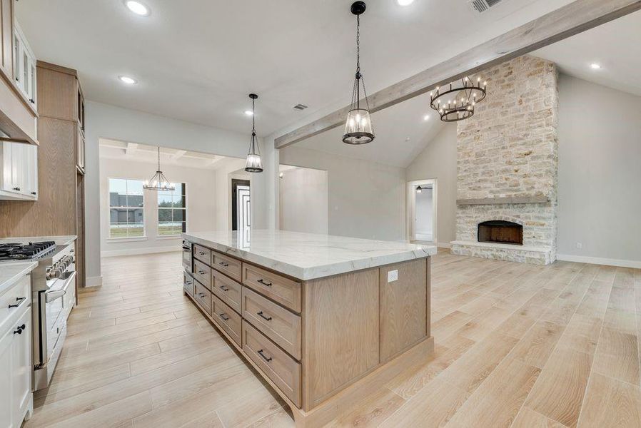 Kitchen with light hardwood / wood-style floors, appliances with stainless steel finishes, hanging light fixtures, vaulted ceiling with beams, and a large island