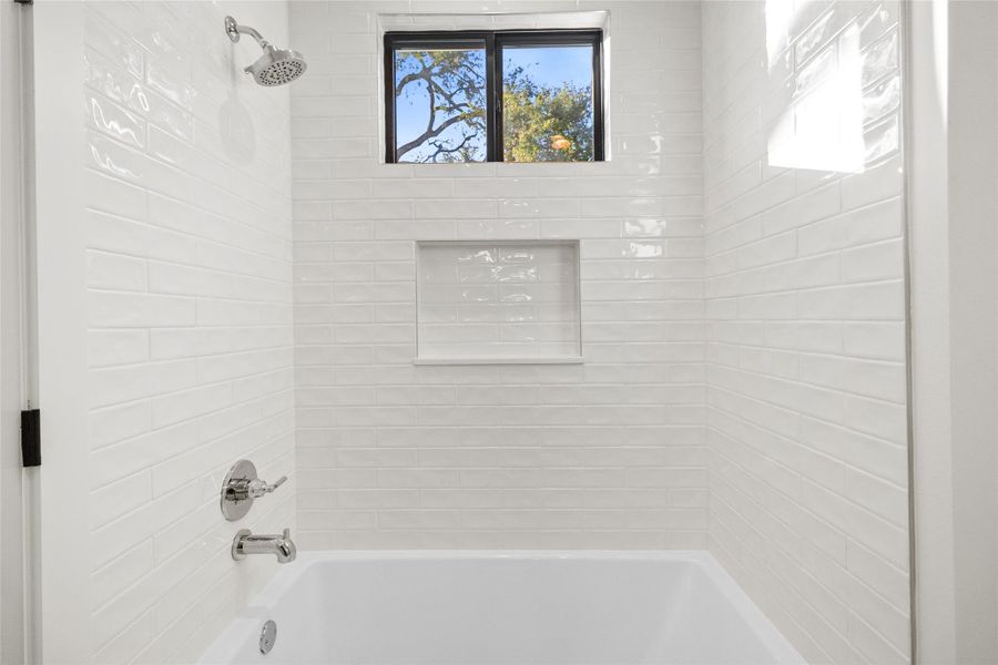 This sleek tub-and-shower combo blends classic style with modern finishes, featuring glossy white subway tile, a built-in niche for toiletries, and a window that brings in natural light while maintaining privacy. It’s a clean, calming space designed for both quick mornings and long, relaxing evenings.