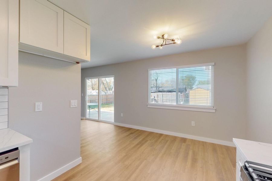 Kitchen with baseboards, light wood-type flooring, white cabinetry, stainless steel dishwasher, and light stone counters