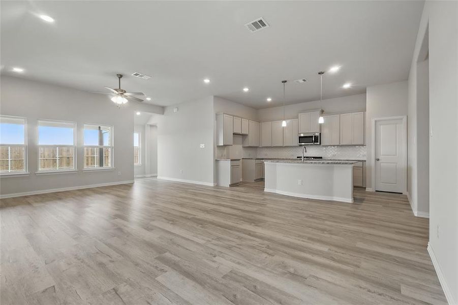 Kitchen featuring open floor plan, a kitchen island with sink, a ceiling fan, decorative light fixtures, and stainless steel microwave Kitchen featuring open floor plan, a kitchen island with sink, a ceiling fan, decorative light fixtures, and stainless steel microwave