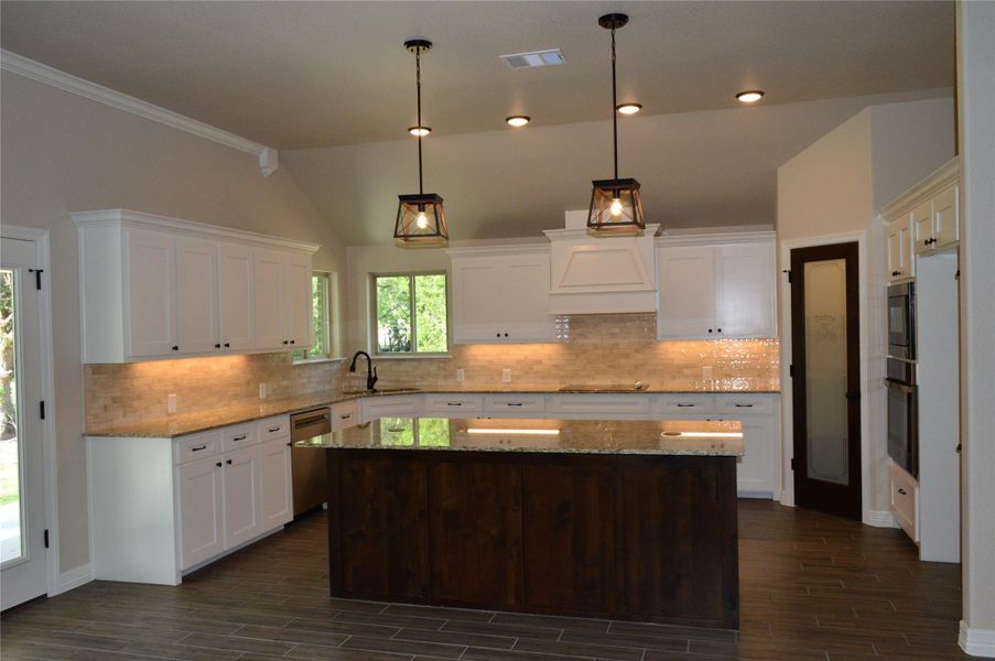 Kitchen with appliances with stainless steel finishes, custom exhaust hood, white cabinets, dark wood-type flooring, and vaulted ceiling