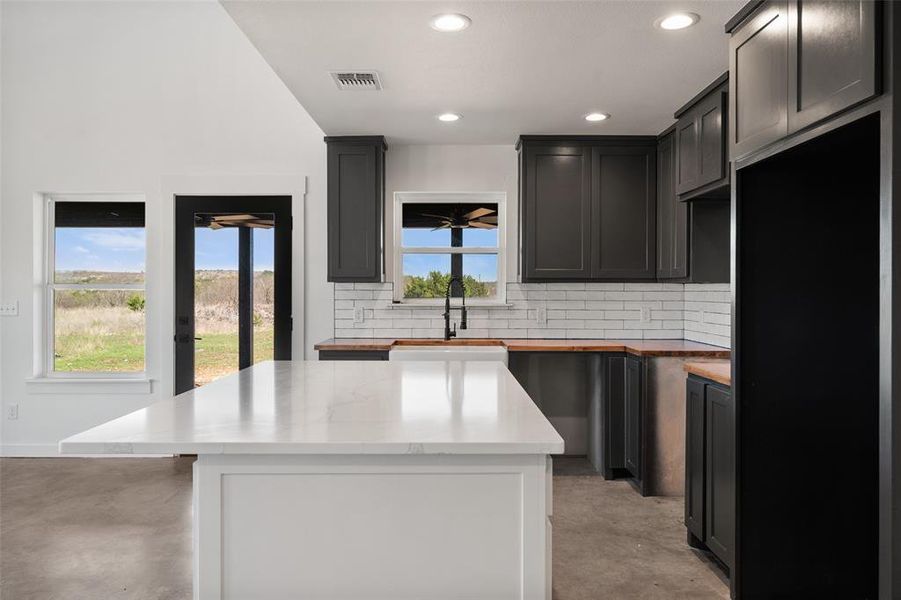 Kitchen with a kitchen island, concrete floors, decorative backsplash, recessed lighting, and butcher block countertops