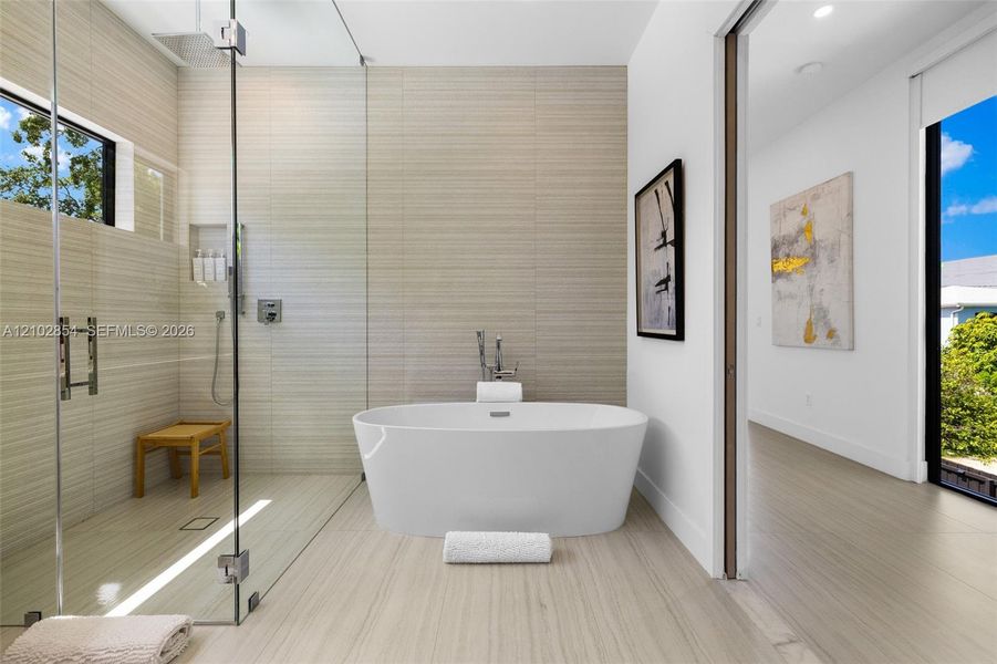 Freestanding soaking tub, walk-in glass-enclosed shower, built-in shower niche, and floor-to-ceiling textured tile wall