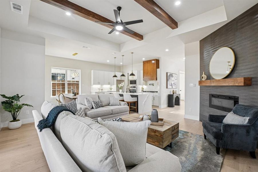 Living room featuring ceiling fan, a fireplace, light wood-type flooring, recessed lighting, and beam ceiling