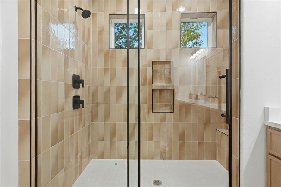 Walk-in shower featuring a matte black rain shower head, vertical stacked tile, and dual built-in shower niches Walk-in shower featuring a matte black rain shower head, vertical stacked tile, and dual built-in shower niches