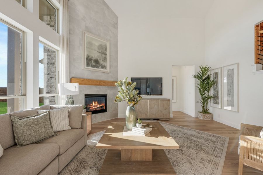 Living room with vaulted ceiling, stone fireplace, hardwood floors, and large windows