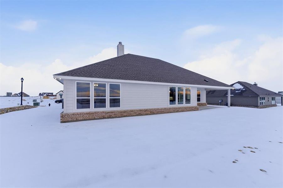 Snow covered house featuring brick siding, a patio area, a chimney, and roof with shingles Snow covered house featuring brick siding, a patio area, a chimney, and roof with shingles