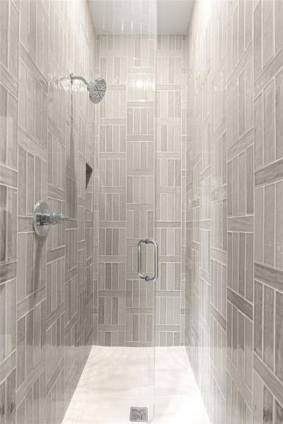 Enclosed shower featuring full-height patterned tile walls, a built-in shower niche, a rain-style shower head, a glass door with a polished chrome handle, and a tiled shower pan