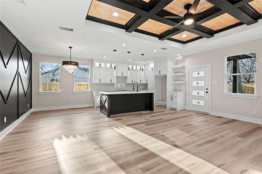 Kitchen featuring pendant lighting, white cabinetry, an island with sink, and coffered ceiling