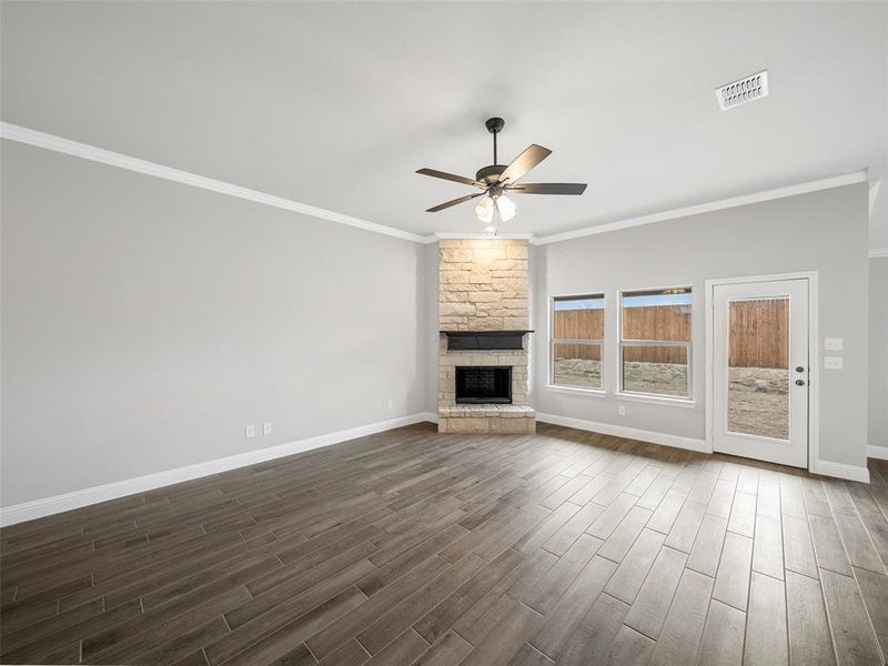 Unfurnished living room featuring dark wood-style floors, baseboards, visible vents, ceiling fan, and a stone fireplace