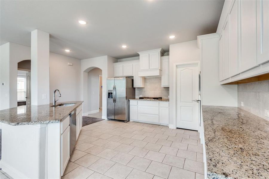 Kitchen with appliances with stainless steel finishes, white cabinetry, backsplash, light stone countertops, and sink