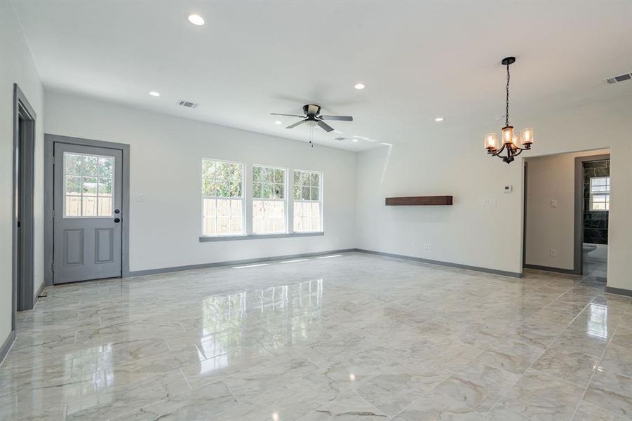 Unfurnished living room with ceiling fan with notable chandelier and light tile patterned floors