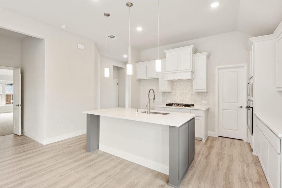 Kitchen with white cabinets, gray island with sink, pendant lights, and light wood floors