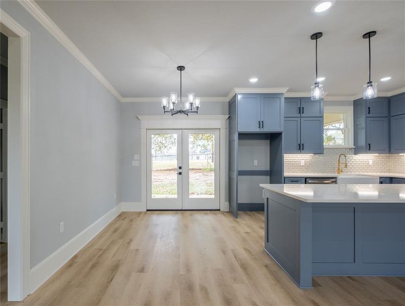 Kitchen featuring blue cabinetry, hanging light fixtures, ornamental molding, light stone countertops, and a chandelier