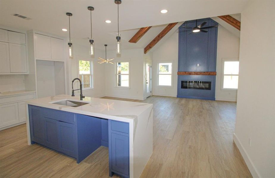 Kitchen featuring beamed ceiling, white cabinets, decorative light fixtures, light wood finished floors, and a large fireplace Kitchen featuring beamed ceiling, white cabinets, decorative light fixtures, light wood finished floors, and a large fireplace