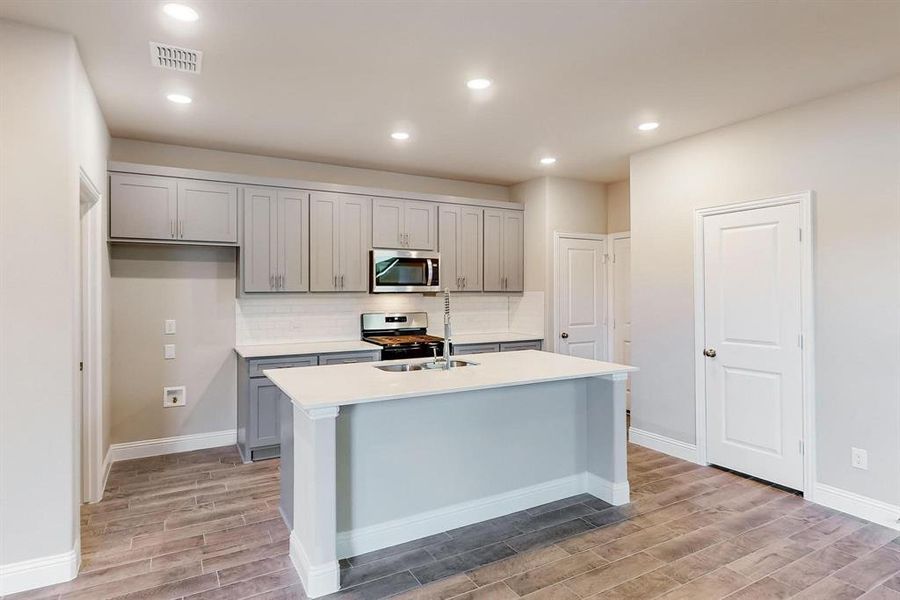 Kitchen featuring gray cabinetry, stainless steel appliances, light hardwood / wood-style flooring, decorative backsplash, and a center island with sink