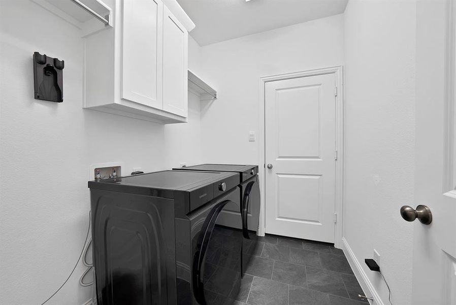Laundry room featuring dark gray tile flooring, crisp white walls, white shaker-style cabinetry, and a wall-mounted shelving unit