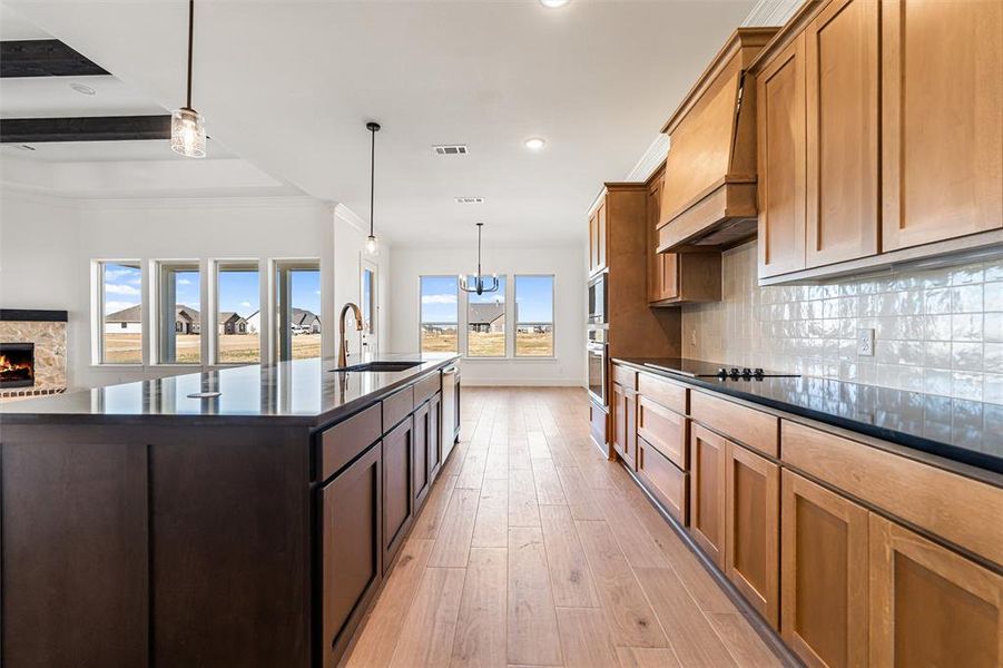 Kitchen featuring decorative light fixtures, light wood finished floors, tasteful backsplash, open floor plan, and a stone fireplace