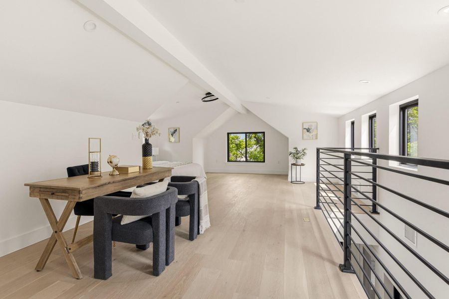 Spacious loft area featuring light wood-finish flooring, white walls, and a vaulted ceiling with exposed beams