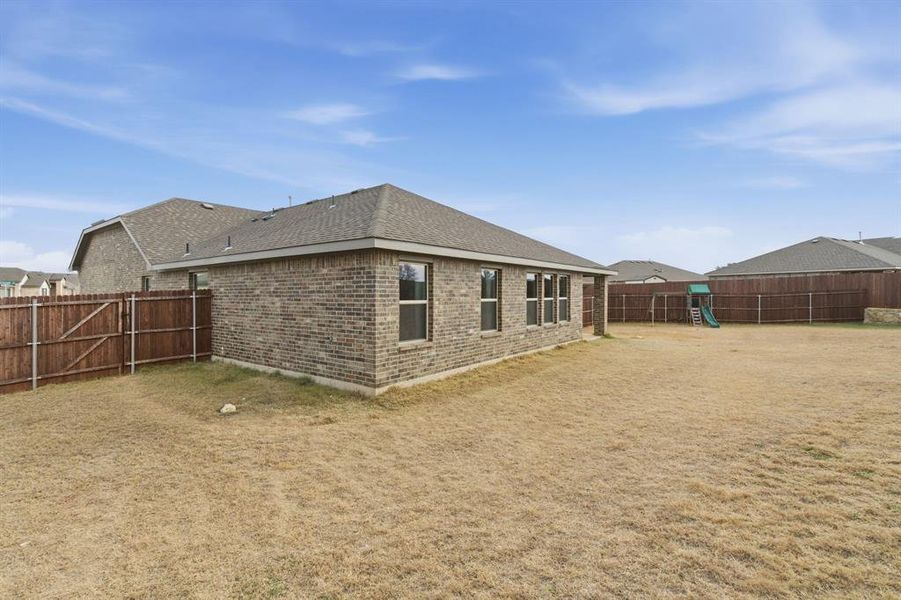 Rear view of house with a fenced backyard, brick siding, a shingled roof, and a playground