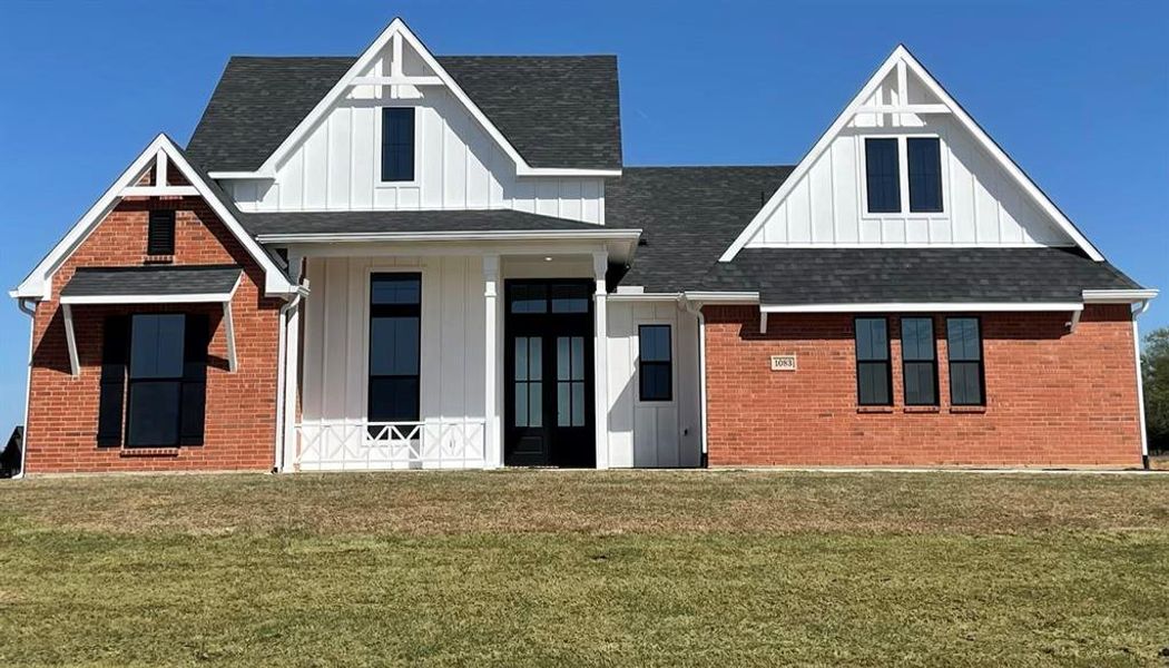 Modern inspired farmhouse featuring board and batten siding, covered porch, a front yard, and a shingled roof