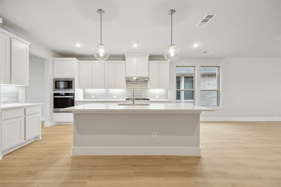 Kitchen featuring built in microwave, white cabinetry, hanging light fixtures, wall oven, and a center island with sink