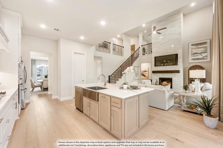 Open-concept kitchen with large island, stainless appliances, and two-story living room with stone fireplace and staircase.