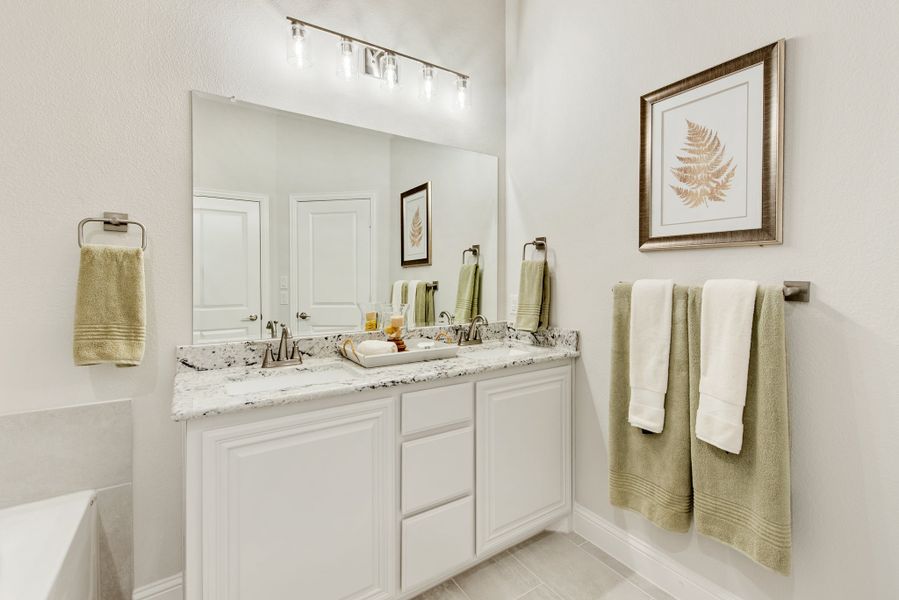 Bathroom with double sink vanity, white cabinets, granite countertop, large mirror, and lighted fixture above Bathroom with double sink vanity, white cabinets, granite countertop, large mirror, and lighted fixture above