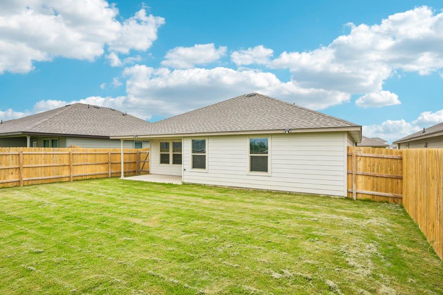 Expansive green lawn surrounds the rear of the property, featuring a private wood fence, a covered patio area, and light-colored siding