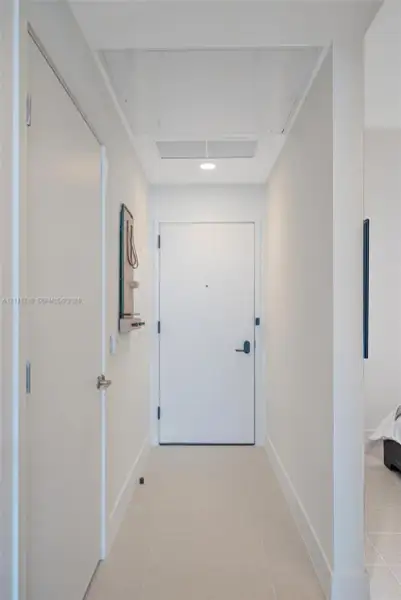Entry hallway featuring neutral tile flooring, smooth-finish walls, a solid-core entry door with integrated peephole, and recessed ceiling lighting