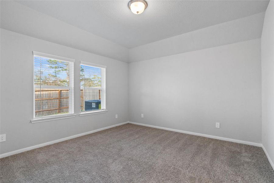 The primary bedroom provides a peaceful escape with a bright, neutral palette, sloped ceilings, large windows, and plush carpet flooring, creating a calm and restorative atmosphere to end your day.