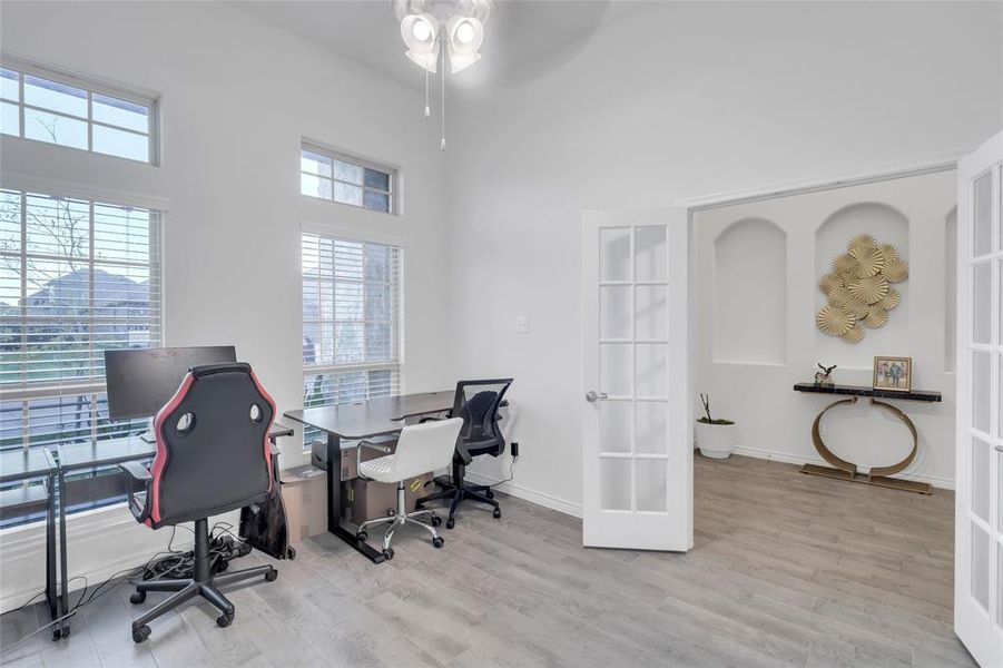 Home office with ceiling fan, a towering ceiling, light hardwood / wood-style flooring, and french doors